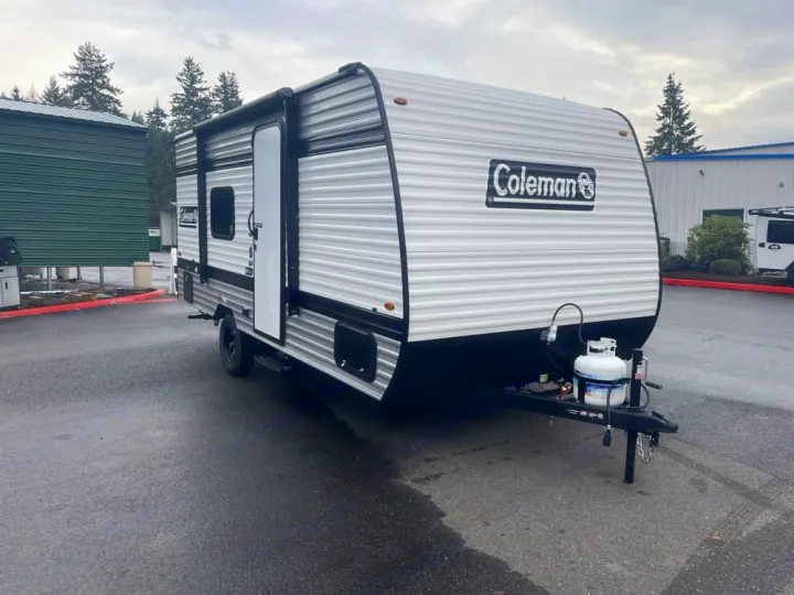 Explore the outdoors! This compact Coleman travel trailer is available for rv rental, parked on asphalt with a propane tank visible.. Keystone RV Coleman 2025