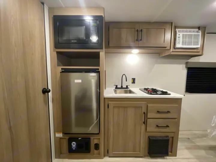 Modern RV rental kitchen with microwave, mini-fridge, sink, stove, and AC unit for comfortable adventures.. Keystone RV Coleman 2025