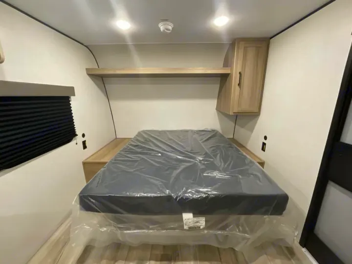 New RV rental bedroom with clean, plastic-covered bed, overhead shelf, and window blinds.. Keystone RV Coleman 2025