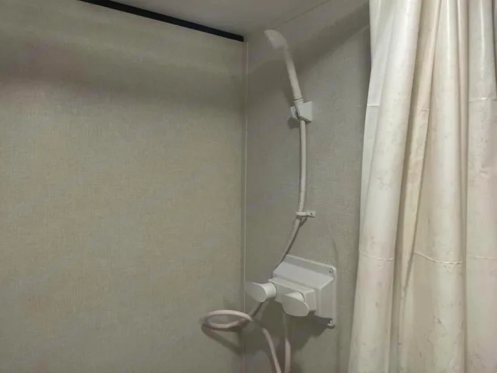 Compact shower in an rv rental, featuring a handheld shower head, dual controls, and a white curtain in a small bathroom space.. Keystone RV Coleman 2025