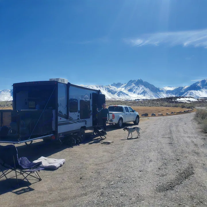 RV rental adventure in snowy mountains. Toy hauler, pickup, and dog on a dirt road. Scenic camping views.. Forest River Cherokee Wolf Pup 2020