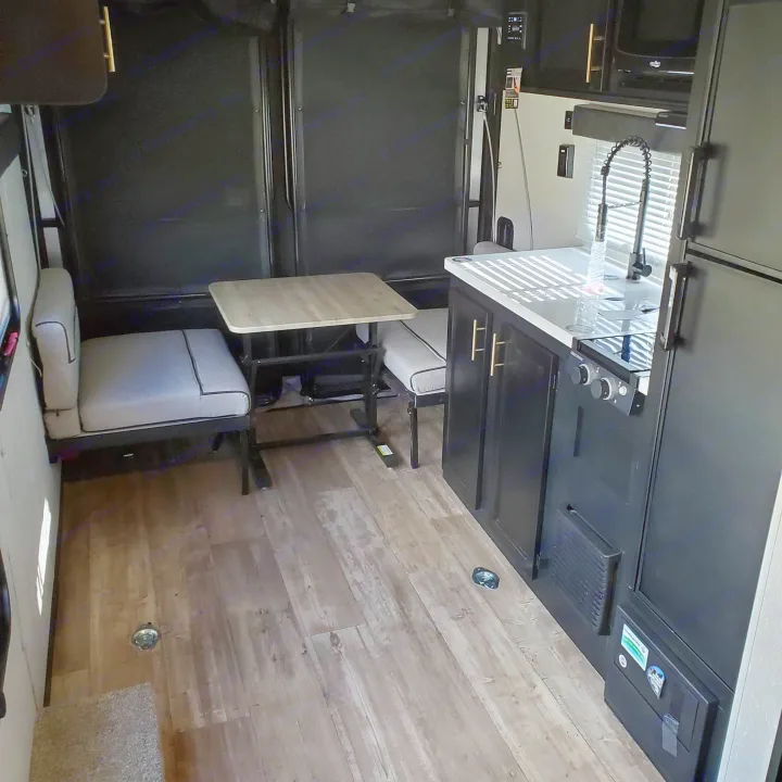 Modern RV rental interior featuring a kitchen with dark cabinets, a dining table, and cozy seating. Light-colored flooring adds contrast.. Forest River Cherokee Wolf Pup 2020