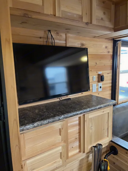 An RV rental's cozy wood interior, featuring a TV, countertop, cabinets, and fishing rod holders. Perfect for ice fishing.. Ice Castle Fish Houses Ice Castle Fish Houses Trailer 2023