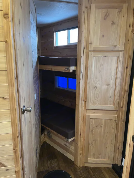 RV rental's rustic interior: wooden bunk beds, bright windows, and ample cabinets. A cozy, compact camper space.. Ice Castle Fish Houses Ice Castle Fish Houses Trailer 2023