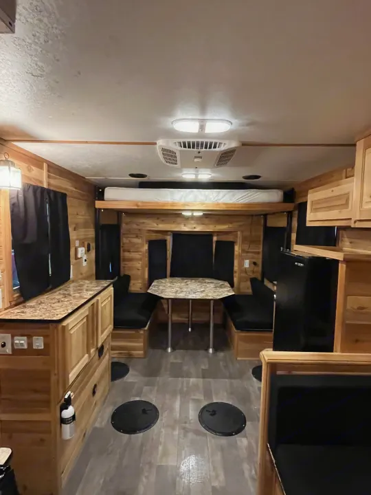 Spacious RV rental interior with wood paneling, dining table, bunk bed, kitchen, and unique floor holes for ice fishing.. Ice Castle Fish Houses Ice Castle Fish Houses Trailer 2020