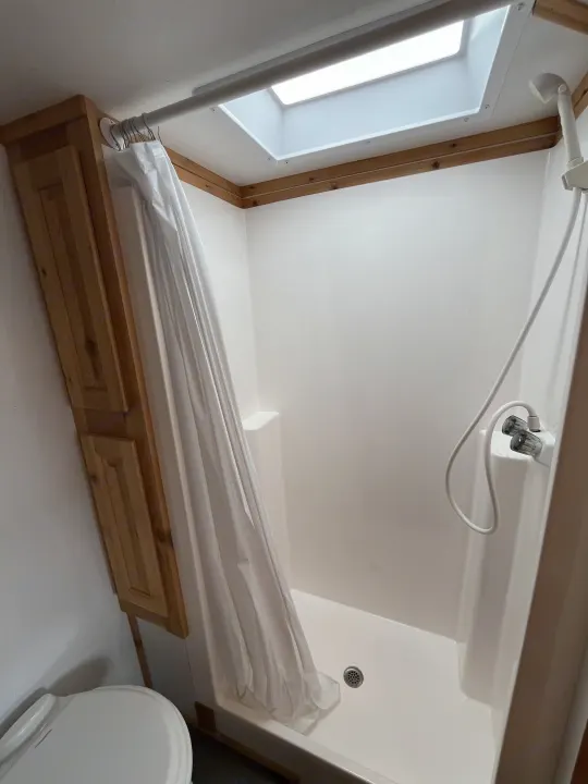 RV rental compact shower: white curtain, skylight, wooden cabinet, and visible toilet seat area.. Ice Castle Fish Houses Ice Castle Fish Houses Trailer 2020
