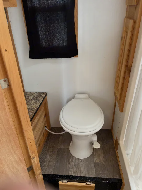 Compact rv rental bathroom featuring a Dometic toilet, wood-look flooring, wood cabinetry, and a shower curtain.. Ice Castle Fish Houses Ice Castle Fish Houses Trailer 2020
