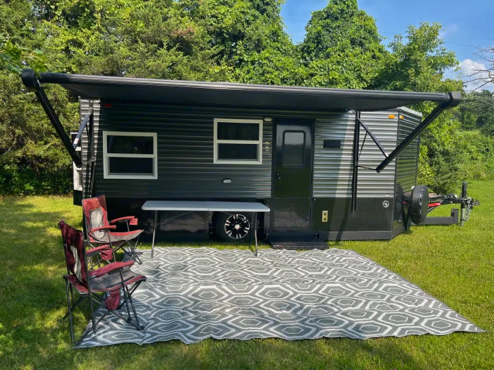 This dark RV rental, with its extended awning, chairs, and patterned rug, offers a comfortable outdoor camping experience.. Ice Castle Fish Houses Ice Castle Fish Houses Trailer 2020