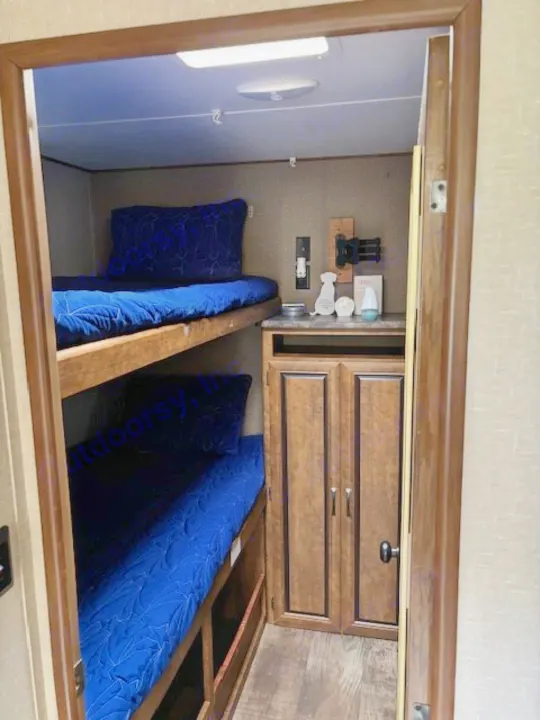 Inside an RV rental: comfortable bunk beds with vibrant blue covers and handy storage cabinetry.. Crossroads RV Zinger 2017