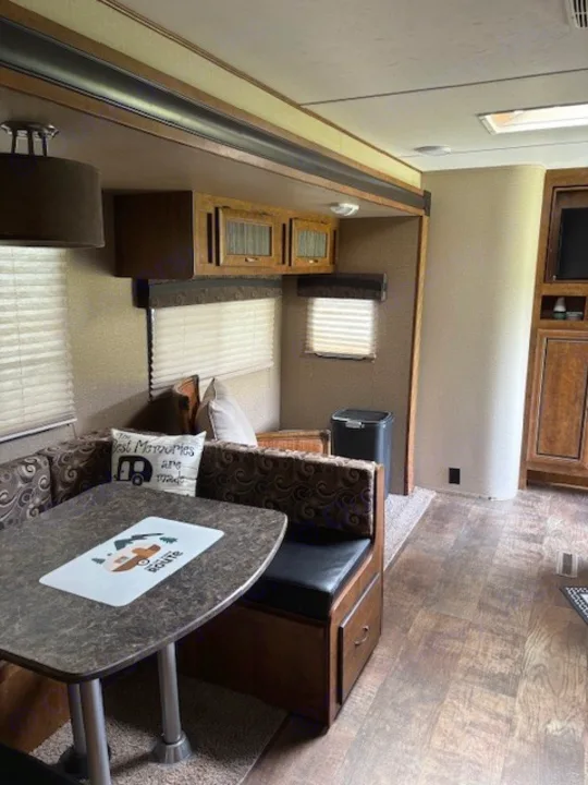 Cozy RV rental dinette with patterned bench seats, a tabletop, overhead cabinets, and blinds, perfect for travel.. Crossroads RV Zinger 2017
