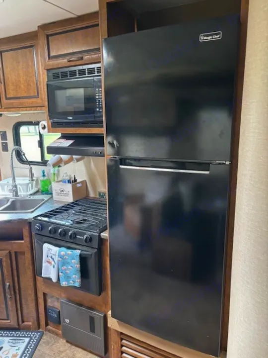 RV rental kitchen featuring a black Magic Chef fridge, gas stove, and microwave, integrated into wooden cabinetry.. Crossroads RV Zinger 2017