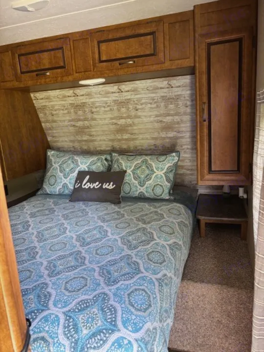Comfortable RV rental bedroom interior with blue patterned bedding, wooden cabinets, and a rustic headboard.. Crossroads RV Zinger 2017
