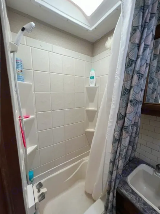 Bright RV rental bathroom with a skylight, showing a compact shower-tub, sink, and patterned curtain.. Crossroads RV Zinger 2017