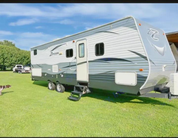 Zinger travel trailer RV rental, grey and black, parked on green grass under a blue sky. Ideal for road trips.. Crossroads RV Zinger 2017