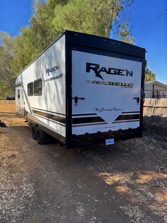 Rear of a white Ragen Overnighter toy hauler with ramp door, an ideal rv rental for outdoor adventures. Parked on dirt.. Genesis Supreme Rv FS2750 2026