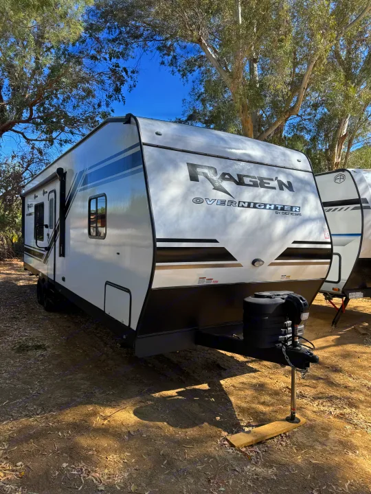 A white Ragen Overnighter toy hauler rv rental parked under trees. Ideal for camping and travel adventures.. Genesis Supreme Rv FS2750 2026