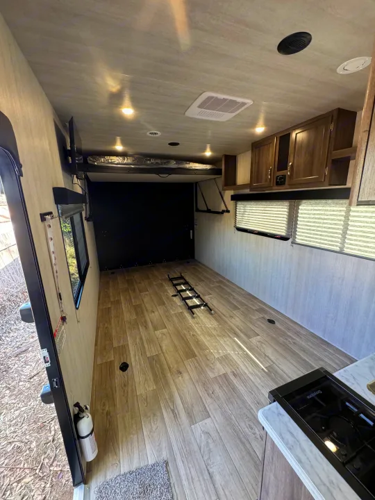 Spacious RV rental toy hauler interior, showing a raised bed, kitchen, open cargo area, and fire extinguisher near the entry.. Genesis Supreme Rv FS2750 2026