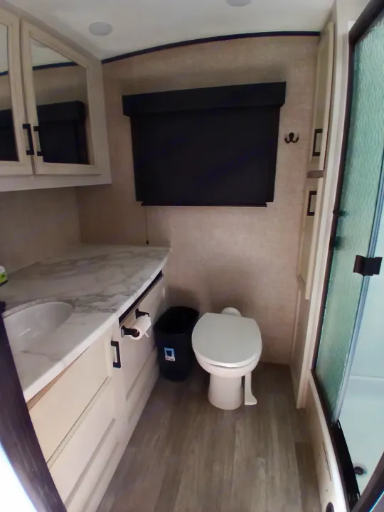 This RV rental bathroom features a sink, toilet, shower stall, mirrored cabinets, and vanity with a light countertop.. Jayco White Hawk 2023