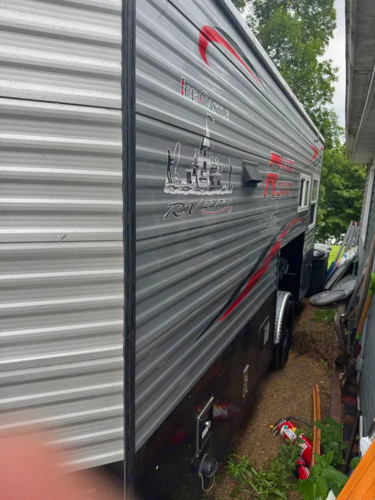 This wet "Ice Castle RV Edition" travel trailer/ice house for rv rental is covered in raindrops, featuring grey siding & red accents.. Ice Castle Fish Houses Ice Castle Fish Houses Trailer 2023