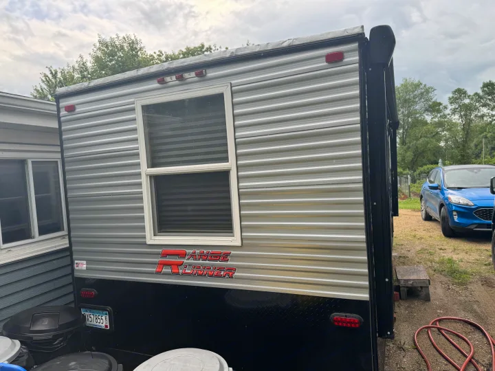 Range Runner travel trailer, ideal for an RV rental, parked outdoors. Side view shows a window and a Minnesota license plate.. Ice Castle Fish Houses Ice Castle Fish Houses Trailer 2023