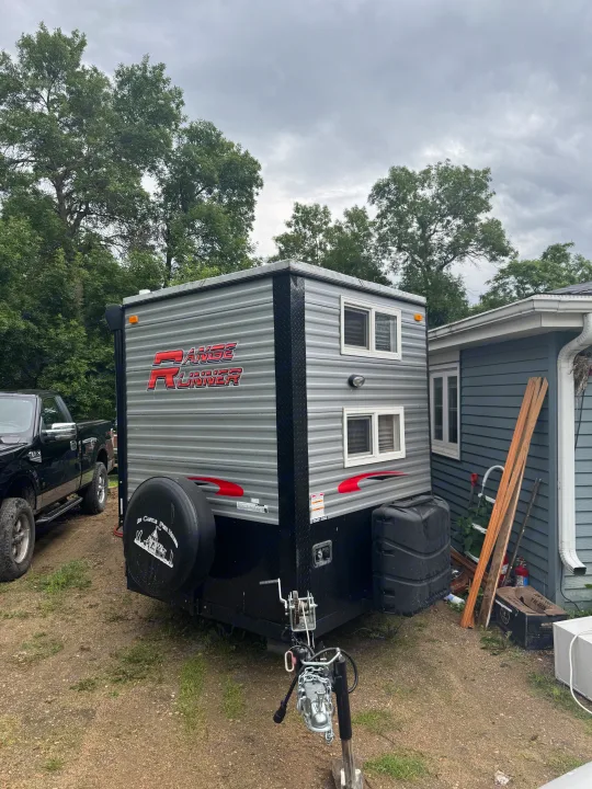 Ice Castle Range Runner ice house (travel trailer) parked outdoors, ready for an RV rental. Truck and house visible.. Ice Castle Fish Houses Ice Castle Fish Houses Trailer 2023