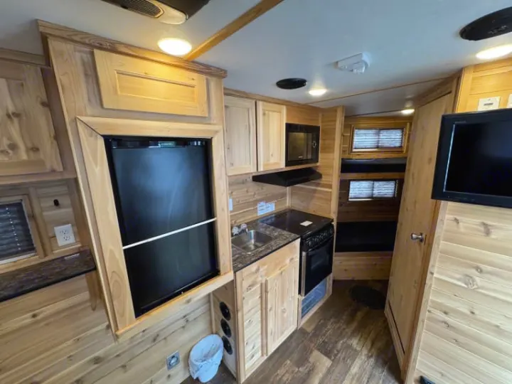 RV rental interior: wood-paneled kitchenette with fridge, stove, microwave, sink, plus bunk beds and TV for compact living.. Ice Castle Fish Houses Ice Castle Fish Houses Trailer 2023