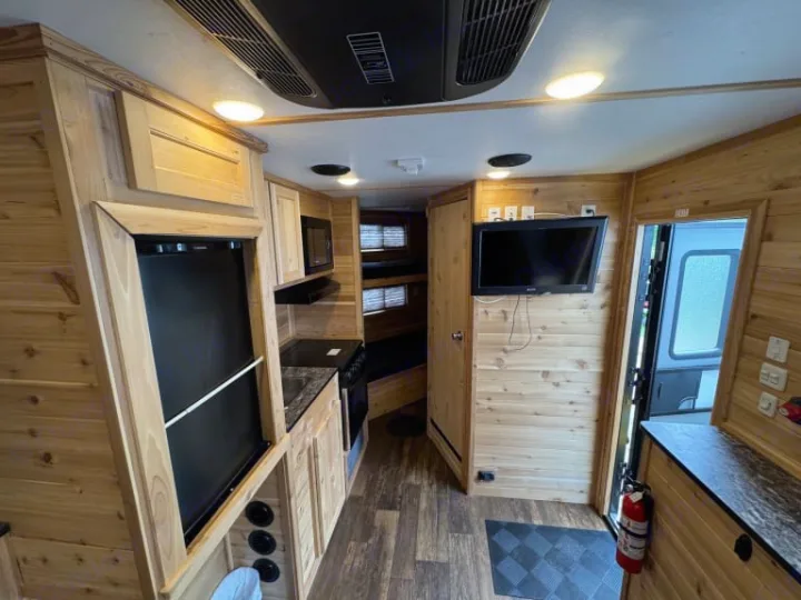 Cozy RV rental interior: full kitchen, fridge, TV, wood paneling, & bunk beds visible. Perfect for your next trip!. Ice Castle Fish Houses Ice Castle Fish Houses Trailer 2023