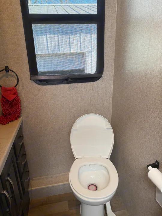 Compact RV rental bathroom: white toilet with red liquid and open lid, screened window, and fluffy red towel on rack.. Jayco Precept 2021