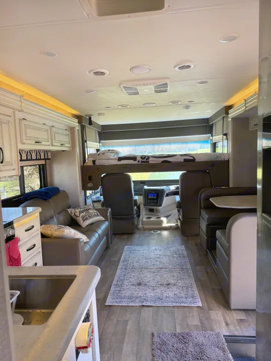 Inviting rv rental interior. View from kitchen to cockpit with overhead bed, sofa, dinette, and stylish rug.. Jayco Precept 2021