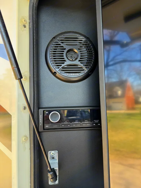 RV rental interior: black panel with Furrion speaker, stereo unit, and gas strut supporting the entry door.. Jayco Precept 2021