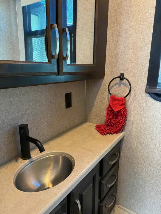 Inside an RV rental, a bathroom with a sleek black faucet, stainless steel sink, grey counter, and a red hand towel.. Jayco Precept 2021