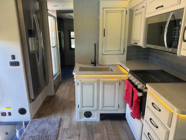 Bright RV rental kitchen with stainless steel appliances, white cabinets, under-cabinet lighting, sink, and stove.. Jayco Precept 2021