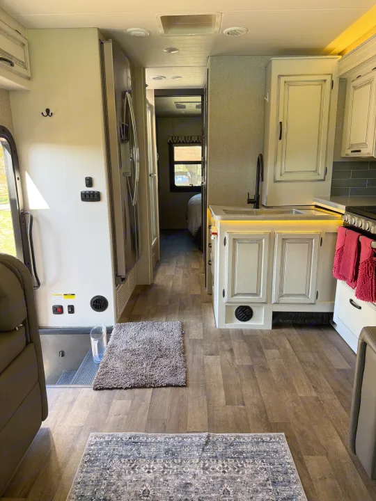 Modern RV rental interior: galley kitchen with light cabinets, hallway to bedroom, wood-look floor with two rugs.. Jayco Precept 2021