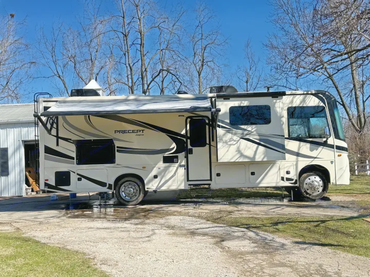 A cream-colored Jayco PRECEPT Class A rv rental parked outside with its awning extended under a clear blue sky.. Jayco Precept 2021