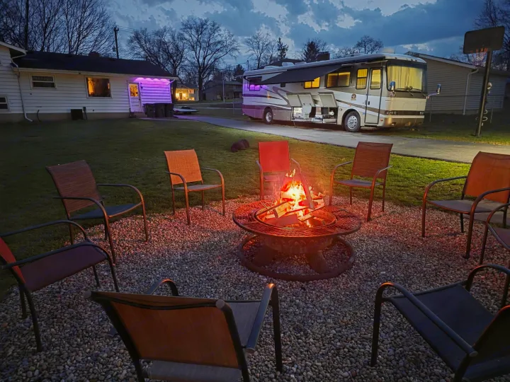 Cozy backyard fire pit evening beside a modern RV rental, perfect for relaxing outdoor adventures under the dusk sky.. Monaco Dynasty 2000