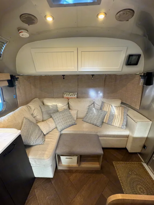 Inviting RV rental lounge area with a light sectional sofa, stylish pillows, and herringbone flooring provides comfort.. Airstream Pottery Barn 2023
