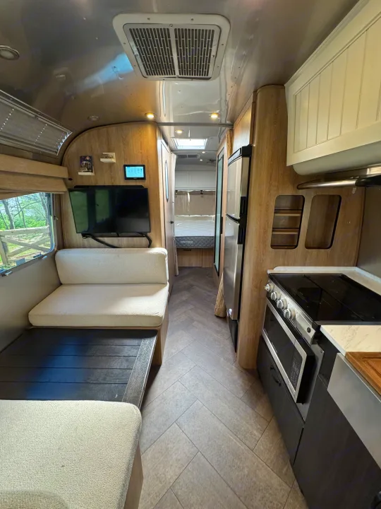 Modern rv rental interior with living area, kitchen, and bedroom. Features metallic ceiling, wood walls, & herringbone floor.. Airstream Pottery Barn 2023