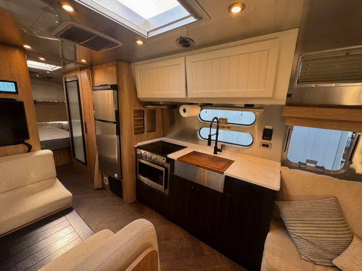 Modern RV rental interior: a sleek kitchen, comfy living space, and cozy bedroom for your adventures.. Airstream Pottery Barn 2023
