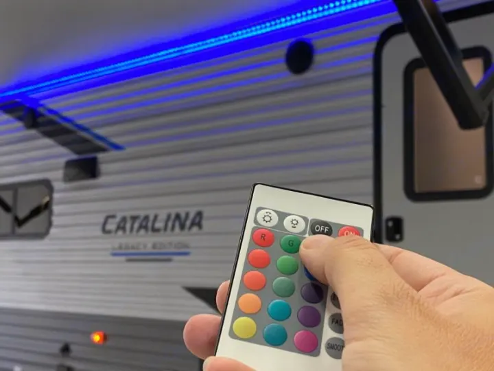 A hand uses a remote to control the blue LED awning lights on a Catalina RV rental, setting the mood for your trip.. Coachmen catalina 2022