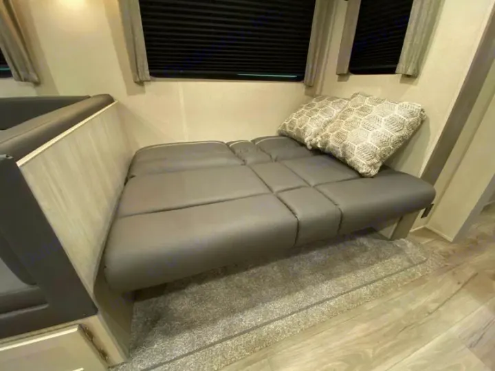 RV rental interior featuring a cozy gray sofa with patterned pillows, window blinds, and light wood-look flooring.. Coachmen catalina 2022