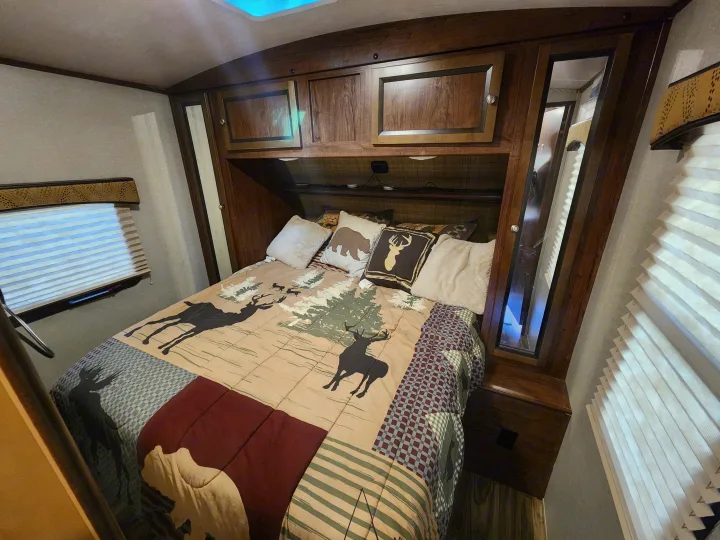 Cozy rv rental bedroom featuring a nature-themed bedspread, wood cabinets, and window blinds for comfort on the road.. Cruiser RV MPG Ultra Lite 2017