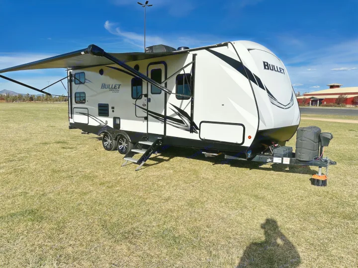 A white Bullet Ultra Lite travel trailer rv rental with an extended awning sits on a grassy field under a blue sky, ready for adventure.. Keystone RV Bullet Ultra Lite 2021