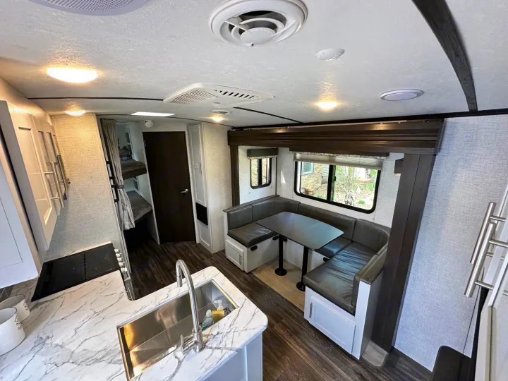 Bright rv rental interior: modern kitchen with marble-look counters, U-shaped dinette, wood-look flooring, and cozy bunk beds.. Keystone RV Bullet Ultra Lite 2021