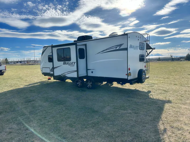 A white travel trailer RV rental parked on a sunny grassy field under a blue sky with clouds, ready for outdoor adventure.. Keystone RV Bullet Ultra Lite 2021