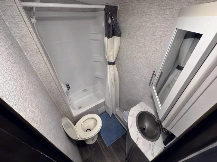 Compact RV rental bathroom with shower/tub, toilet, sink, and mirror. Clean and functional for travel.. Keystone RV Bullet Ultra Lite 2021