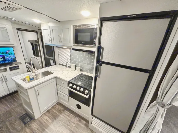 Modern RV rental kitchen featuring a Dometic fridge, microwave, stove, sink, light gray cabinets, and marble countertops.. Keystone RV Bullet Ultra Lite 2021