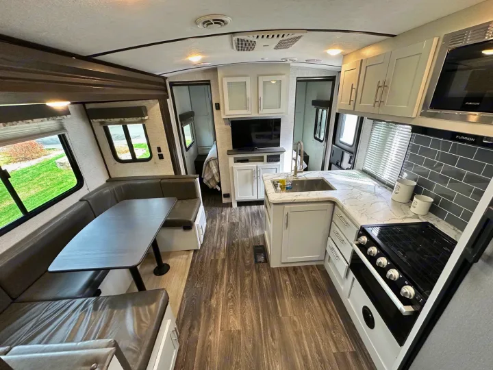 Modern rv rental interior with a bright kitchen, U-shaped dinette, and entertainment center, perfect for travel.. Keystone RV Bullet Ultra Lite 2021