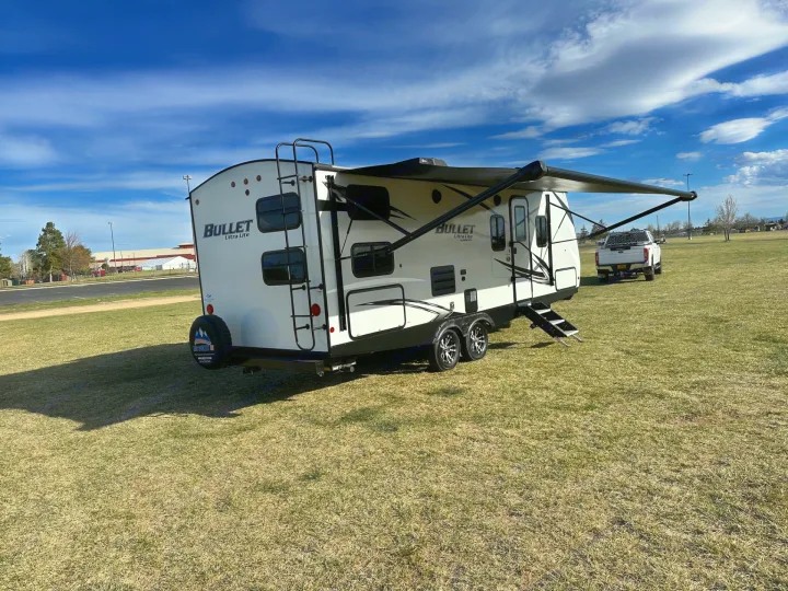 Bullet Ultra Lite travel trailer with awning extended, parked on grass. Ideal for your next RV rental adventure.. Keystone RV Bullet Ultra Lite 2021