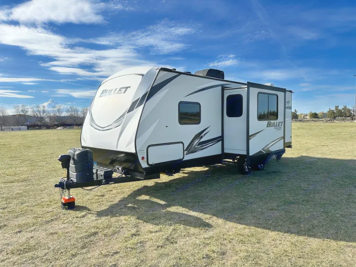 White and black Bullet Ultra Lite travel trailer parked on a grassy field under a blue sky. Perfect for your next rv rental adventure!. Keystone RV Bullet Ultra Lite 2021