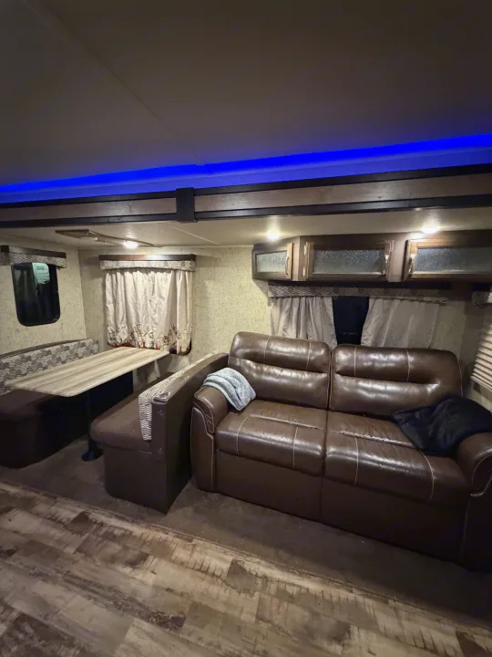 Cozy RV rental interior featuring a brown leather sofa, dinette area, and atmospheric blue LED lighting for comfortable travel.. Forest River Palomino Puma 2018